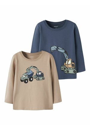 Deux chemises pour enfants à manches longues, une beige avec un motif de camion-benne et d’excavatrice, une bleue avec un grand motif d’excavatrice à l’avant.
