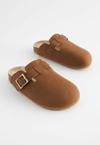 Brune slip-on klipklapper med spænder, overdel i læderlignende materiale, korkfodbed og gummisåler på hvid baggrund.