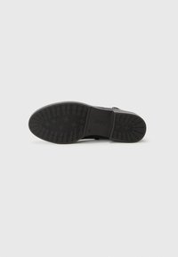 Semelle de chaussure en caoutchouc noir avec un motif texturé de rainures et de crêtes pour une meilleure adhérence, comportant un logo imprimé et des détails de design minimalistes.