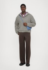 Pull rayé noir et blanc, coupe ample, avec un col montant. Associé à un pantalon marron et un sac bandoulière bleu. Les chaussures sont noires.