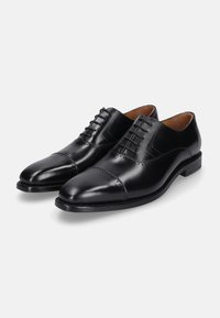 Schwarze Leder Schnürschuhe mit einer Kappenzehe, glatter Oberfläche und dezenten Perforationsdetails entlang der Nähte. Gummisohle.