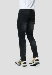 Čierne cargo nohavice s úzkym strihom, vybavené bočnými vreckami a mierne opotrebovanou textúrou. Kombinované s čierno-bežovými športovými topánkami.