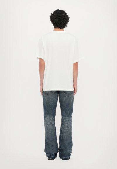 T-shirt blanc à manches courtes avec une coupe décontractée, associé à un jean évasé bleu délavé. Tissu lisse, design simple, sans motifs ni ornements.