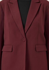 Bordeauxkleurig colbert met één knoop, inkeping revers en klepzakken, gedragen over een zwart topje.