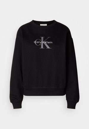 Crni dukserica od pamuka, s okruglim izrezom i slobodnim krojem. Na prednjoj strani prikazuje veliki sivi logo s natpisima "Calvin Klein" i "CK".