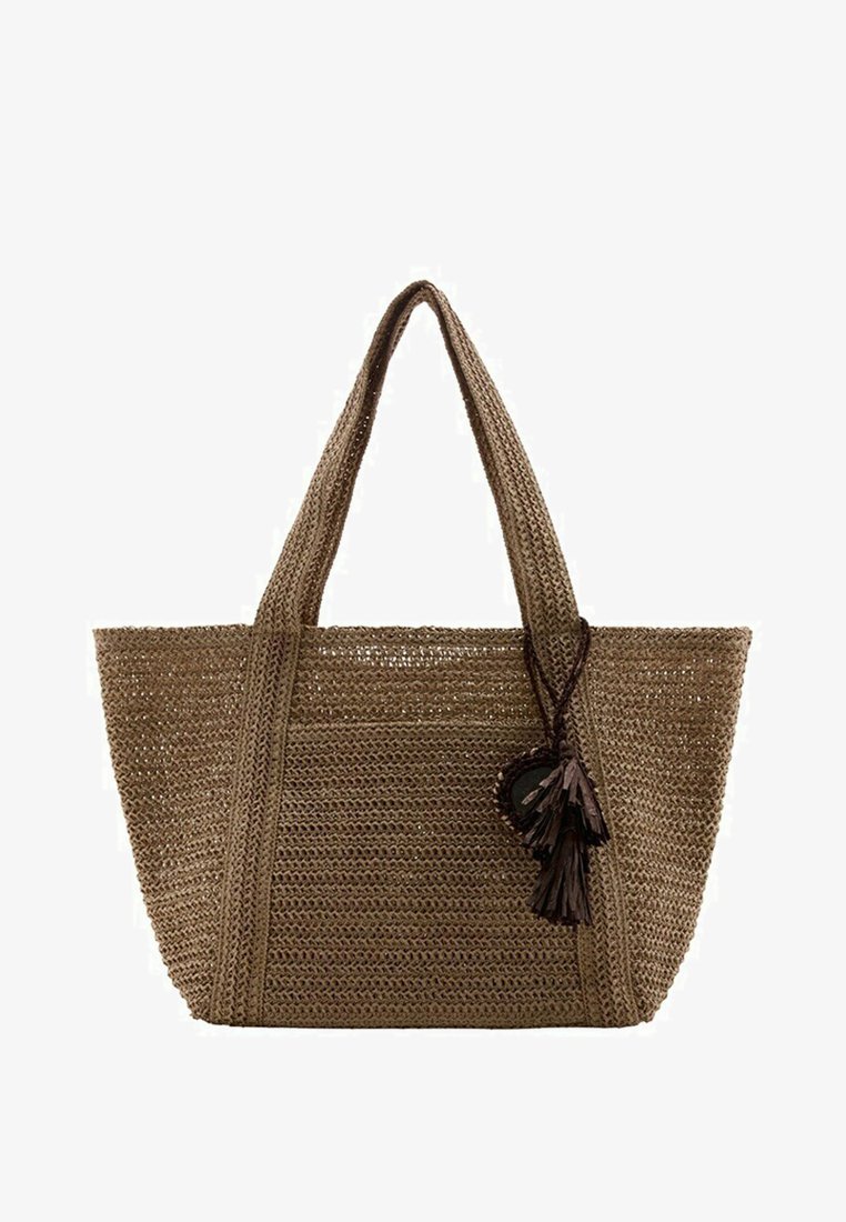 Sac cabas tissé marron avec deux poignées et des pompons décoratifs suspendus à une poignée.