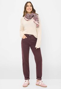 Maglione beige peloso, pantaloni in corduroy bordeaux, sciarpa rosa a fantasia e sneakers rosa chiaro con lacci bianchi. Outfit casual con una vestibilità rilassata.