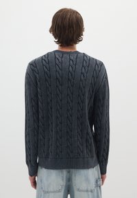 Maglione lavorato a maglia in grigio scuro, con colletto e polsini a coste. Presenta motivi testurizzati verticali e una vestibilità rilassata.