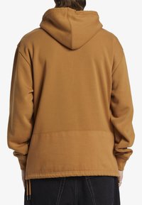 Felpa con cappuccio marrone realizzata in tessuto liscio, con una vestibilità comoda, tasca a marsupio e polsini a coste. La vista posteriore mostra il cappuccio e le cuciture.