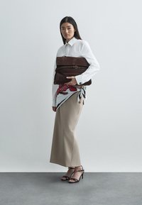 Braune Lederhandtasche mit horizontalem Reißverschluss und Schnalle, getragen mit einem weißen Hemd, einem hellbeigen Rock und schwarzen Riemchen-High Heels, ergänzt durch einen gemusterten Schal.