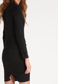 Czarna sukienka denimowa o dopasowanym kroju, z długimi rękawami, paskiem w talii i długości do kolan. Posiada rozcięcie oraz tylne kieszenie.