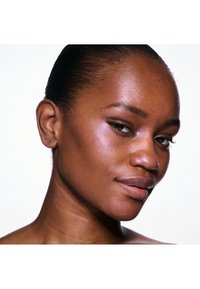 Gros plan sur un visage avec une peau lisse, un maquillage naturel et des reflets brillants. Les traits incluent des pommettes hautes, des lèvres pleines et une queue de cheval noire.