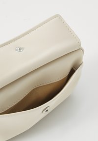Pochette en cuir beige avec une texture lisse, fermeture à clapet magnétique et un design simple, présentant un intérieur en tissu tan contrasté.