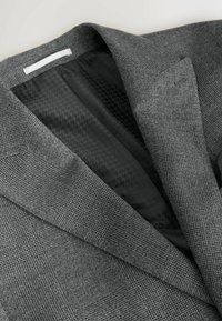 Sivý kockovaný blejzer s čiernym vzorovaným podšívkou, vybavený výrezovým klopovým golierom, zobrazený na neutrálnom pozadí.