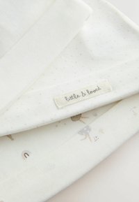 Tessuto di cotone color crema con una texture liscia, presenta un motivo a pois sottile e illustrazioni colorate di ombrelli e arcobaleni. Etichetta visibile.