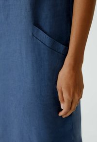 Navy-blaues Leinenkleid mit einer Seitentasche und glatter Textur, teilweise mit einer Hand, die gegen den Stoff gehalten wird, um die Größe zu zeigen.