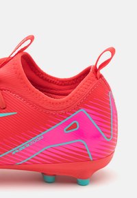 Chaussure de sport rouge avec une tige synthétique texturée, des accents rose et turquoise, un bout rond et une semelle en caoutchouc avec des crampons.