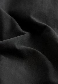 Tissu noir avec des plis doux et une surface légèrement texturée à la lumière naturelle.