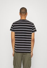 T-shirt à manches courtes rayé noir et blanc, doté d'un col rond et d'une coupe décontractée. Le tissu semble doux avec une texture minimale.
