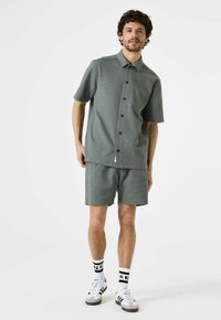 Lichtgroene T-shirt met korte mouwen en bijpassende short van textuurstof. Knopsluiting aan de voorkant, gladde details, gecombineerd met witte sokken en sneakers.