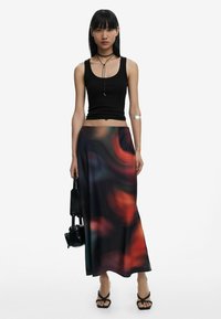 Black tank top, flowing maxi skirt with abstract red and blue patterns, a silver arm cuff, black handbag, and strappy black sandals.