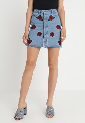 Jupe en denim avec un ourlet effiloché, ornée de broderies de roses rouges et de feuilles vertes, fermeture à boutons à l'avant et taille haute.