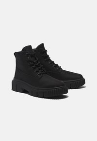 Botas negras hasta el tobillo, fabricadas con un acabado texturizado, que cuentan con suelas de goma gruesas, cordones redondos y un logotipo lateral.