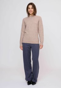 Maglione beige a maglia con collo rotondo, abbinato a pantaloni a righe blu navy. L'outfit presenta una vestibilità comoda e una consistenza morbida.