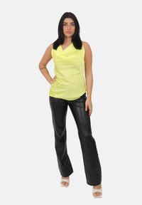 Gul satin ærmeløs top med draperet halsudskæring, kombineret med sorte, højtaljede bukser i imiteret læder og klare hælede sandaler.