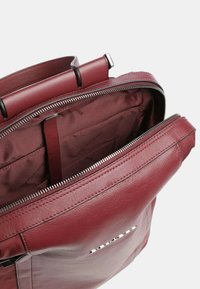 Mochila de cuero burdeos con una textura suave, cierre de cremallera y múltiples compartimentos internos para organización. Cuenta con un asa superior.