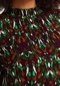 Mönstrad topp med samlad halsringning. Har en livfull design i mörkgrön, brun, vit och djup röd färg. Slät tygstruktur.