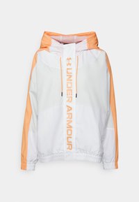 Veste légère blanche et orange avec capuche, dotée de poignets élastiques, d'un ourlet avec cordon de serrage et d'un grand texte "UNDER ARMOUR" à l'avant.