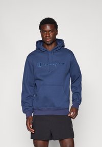 Felpa blu navy realizzata in tessuto morbido, con tasca frontale, cappuccio con lacci e logo "Champion" ricamato in un colore contrastante.