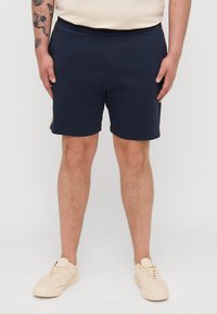 Marinblå shorts i mjukt material, med elastisk midja och en avslappnad passform. Inkluderar sidofickor och uppvikta fållar.
