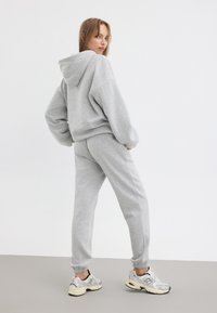 Grå huvtröja och matchande joggers i mjukt tyg. Outfitten har en avslappnad passform, elastiska ärmar och sidofickor. Accentuerad med sneakers.
