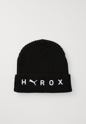 Melnā adīta cepure ar ribotu tekstūru. Uz locītās malas ir balti izšūti burti "HYROX" un Puma logotips.