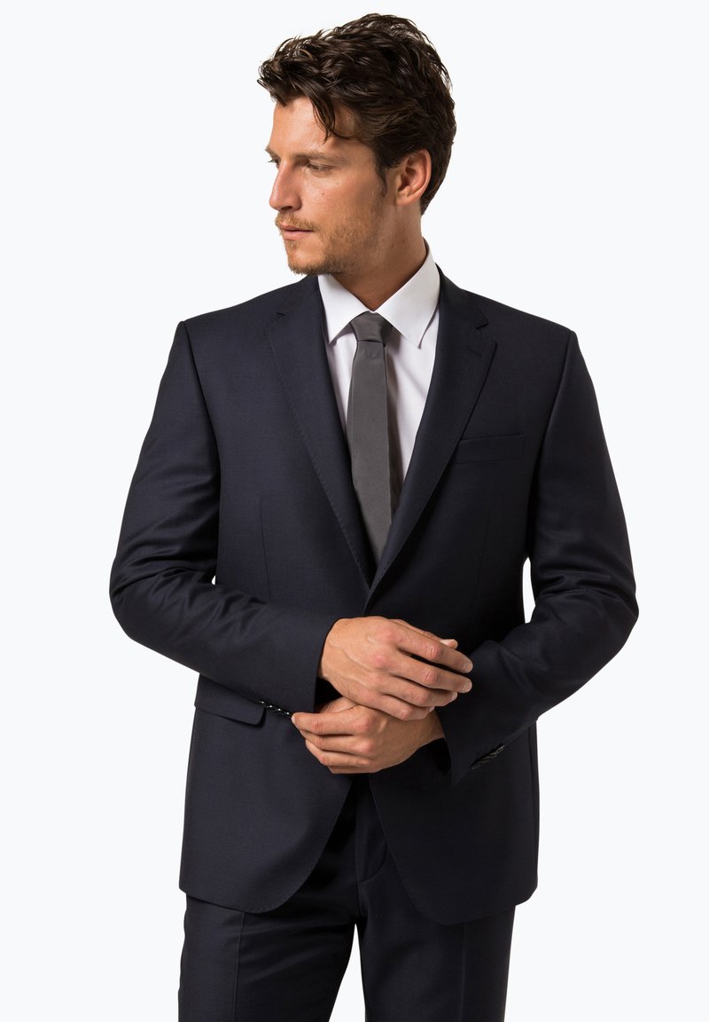 Marineblaues Anzug aus strukturiertem Stoff, mit Schalkragen, Ein-Knopf-Verschluss und schmal geschnittenen Hosen. Kombiniert mit einem hellen Hemd und einer dunklen Krawatte.