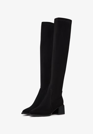 Bottes noires montantes jusqu'aux genoux avec talons blocs et bouts pointus, présentant un tissu lisse et des détails subtils de couture.