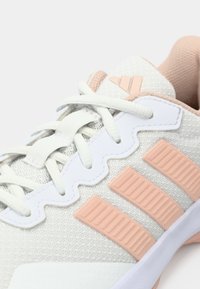 Primo piano di una sneaker Adidas bianca e rosa chiaro che mostra i lacci, il tessuto testurizzato e le iconiche tre strisce laterali.