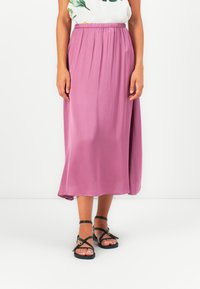 Lyselilla, mid-length skjørt med elastisk midjebånd, laget av mykt stoff. Kombinert med svarte sandaletter med stropper og en blomstret topp.