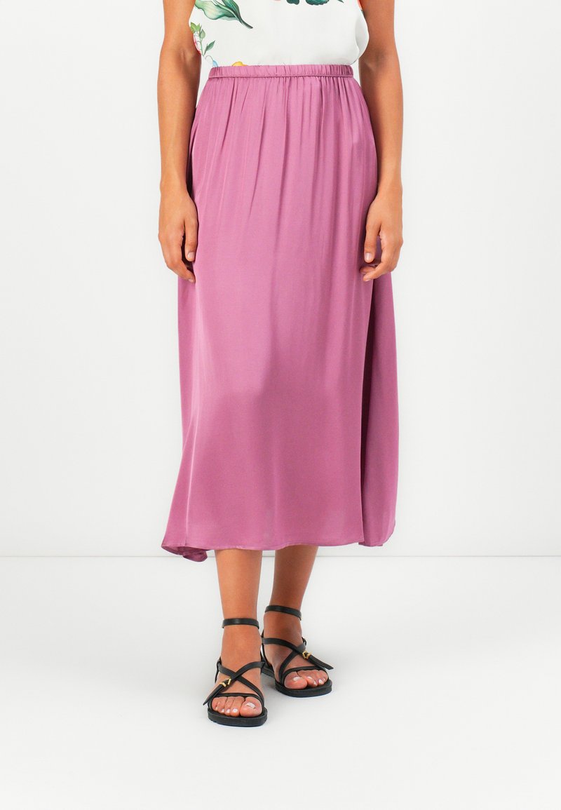 Lyselilla, mid-length skjørt med elastisk midjebånd, laget av mykt stoff. Kombinert med svarte sandaletter med stropper og en blomstret topp.