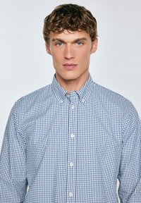 Camisa de cuadros azul y blanca con cuello, hecha de material de algodón y con un corte clásico. Los botones son blancos y están espaciados de manera uniforme.