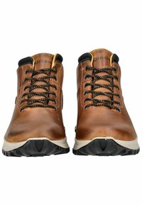 Botas de cuero marrón de media caña con cordones negros, acabado texturizado, suelas de goma y acentos en contraste en color beige. Cuenta con un cuello acolchado y ojales.