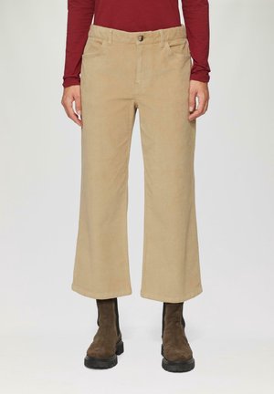 Béžové manšestrové kalhoty s širokými nohavicemi, nošené s hnědými kotníkovými botami a dlouhým rukávem vínového topu, zobrazené od pasu po nohy.