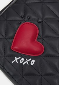 Černá prošívaná syntetická taška s červenou koženou nášivkou ve tvaru srdce a bílým nápisem "xoxo", s texturovanými povrchovými detaily.
