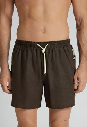 Pantalones cortos marrones de hombre con cordón, cintura elástica y un abrebotellas de metal sujeto al aro del lado derecho.