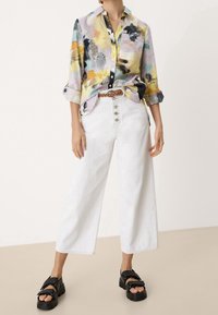 Värikäs, kuviollinen pitkähihainen paita, jossa on napitettava etu, yhdistetty korkeavyötäröisiin valkoisiin leveälahkeisiin farkkuihin ja mustiin korokepohjaisiin sandaaleihin.