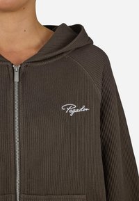 Brunhood z zamkiem błyskawicznym i prążkowanym wykończeniem, z kapturem na sznurku, z białym logo na lewej piersi oraz dwoma przednimi kieszeniami.