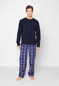 Marineblauwe longsleeve top gecombineerd met blauwe geruite slaapbroek met witte en zwarte accenten. Lichtgewicht stof, ontspannen pasvorm en open manchetten.