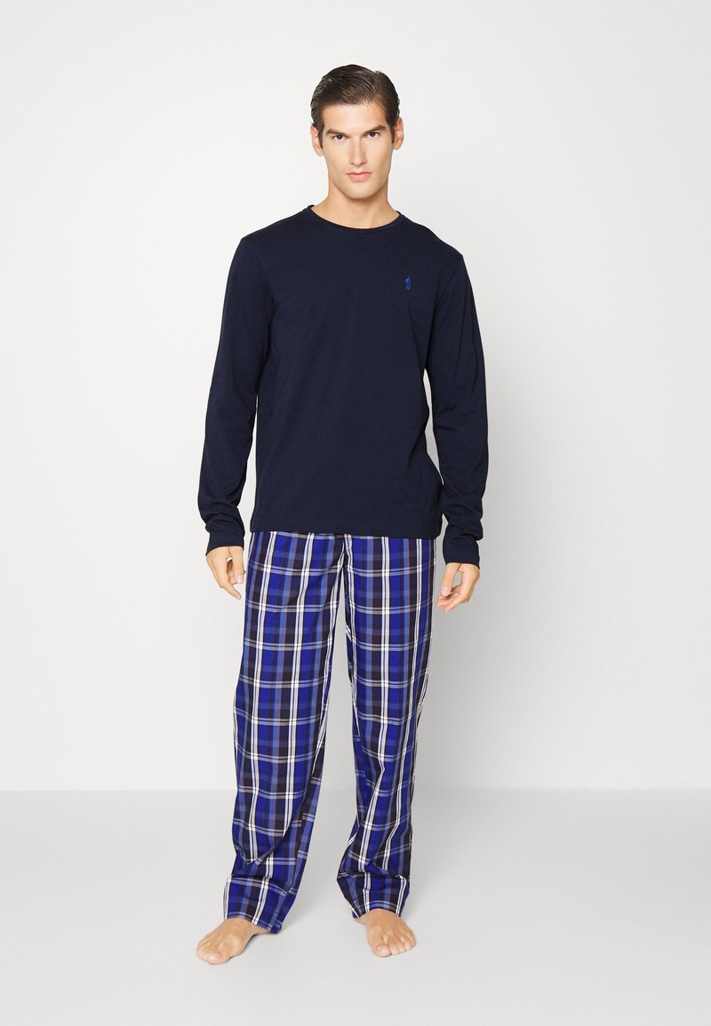 Marineblauwe longsleeve top gecombineerd met blauwe geruite slaapbroek met witte en zwarte accenten. Lichtgewicht stof, ontspannen pasvorm en open manchetten.